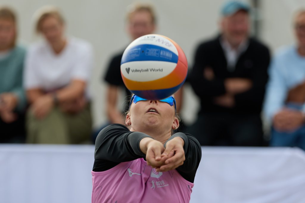 En spiller i beachvolleyball prøver å motta ballen under en kamp, med tilskuere i bakgrunnen.