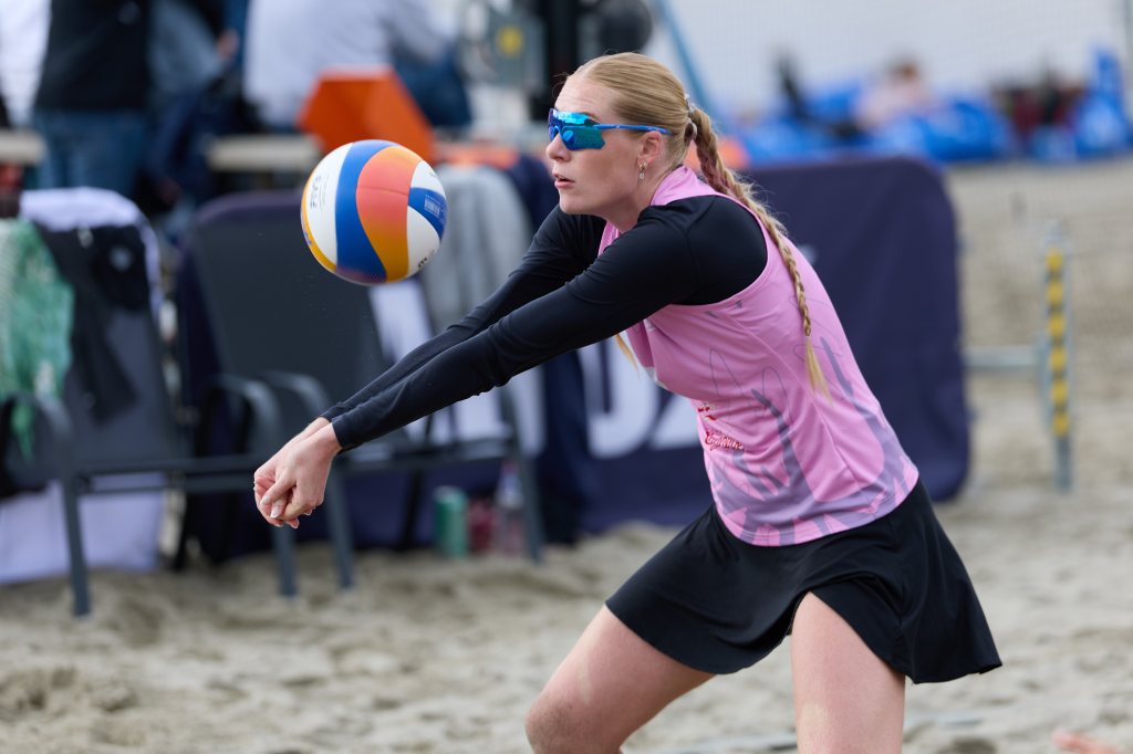 En kvinnelig volleyballspiller i rosa drakt og solbriller utfører en mottak i sanden.