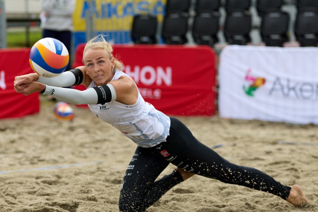 En kvinnelig sandvolleyballspiller som utfører en forlengs dykking for å ta imot ballen på en sandbane.
