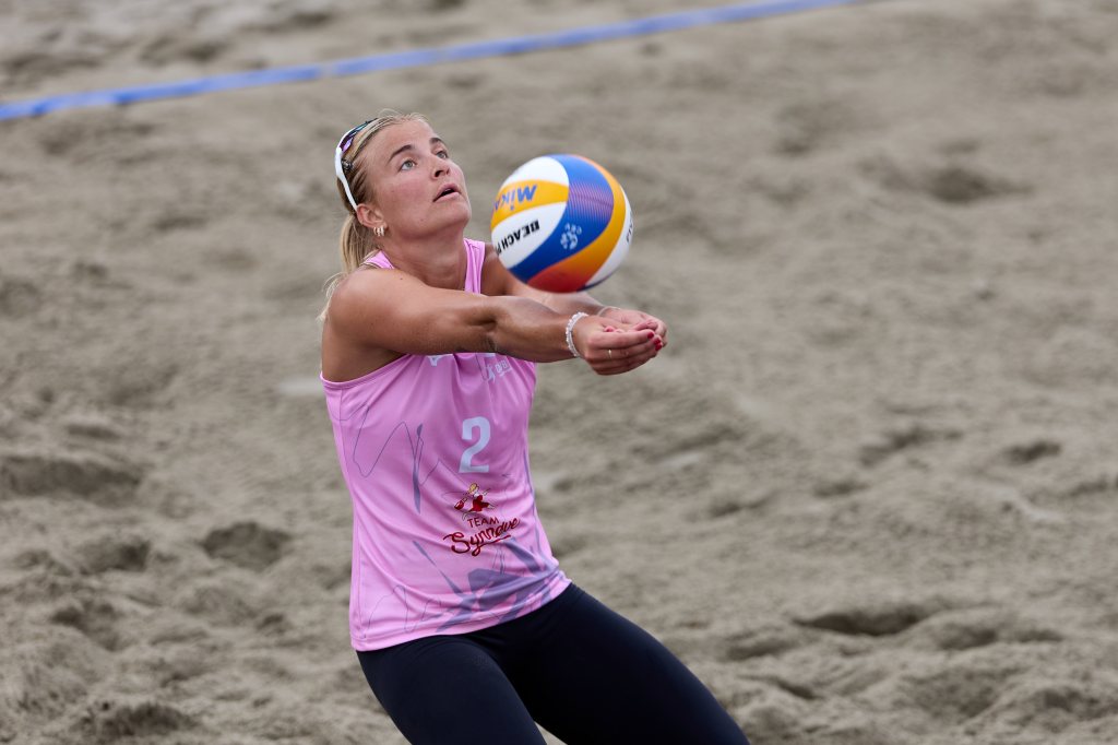 En kvinne i treningstøy spiller sandvolleyball, mens hun ser opp mot en volleyball som kommer mot henne.