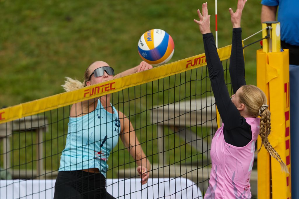 To volleyballspillere som konkurrerer under en kamp. Den ene spilleren hopper opp for å slå ballen, mens den andre prøver å blokkere den ved nettet.