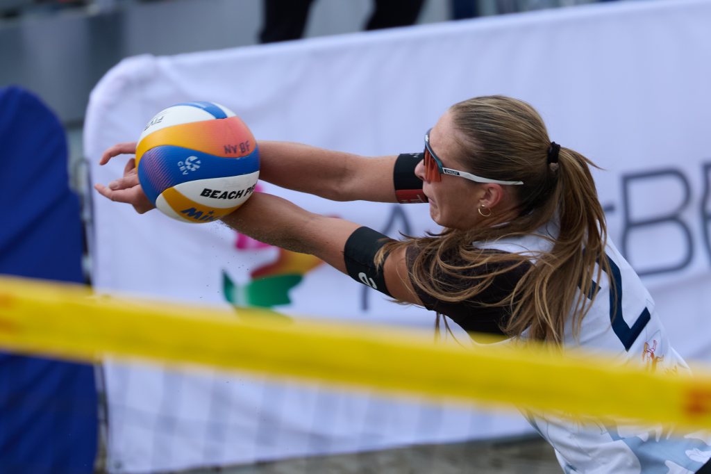 En kvinne i sportsklær strekker seg for å spille volleyball i sand.