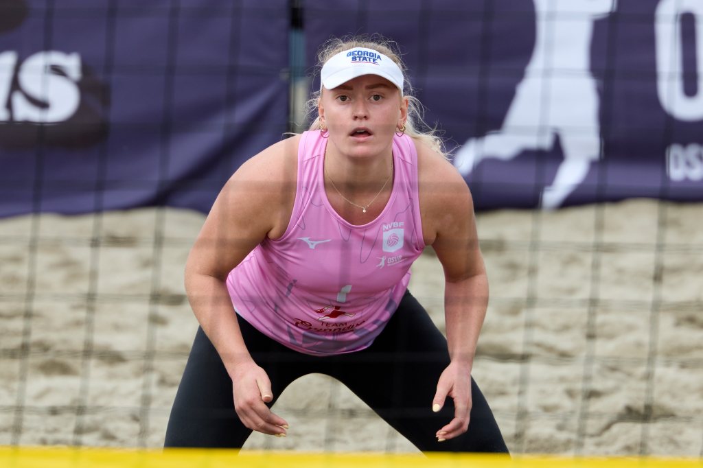 En kvinne i rosa volleyballtrøye og svart bukser, ser fremover fra sandvolleyballbanen under en kamp.
