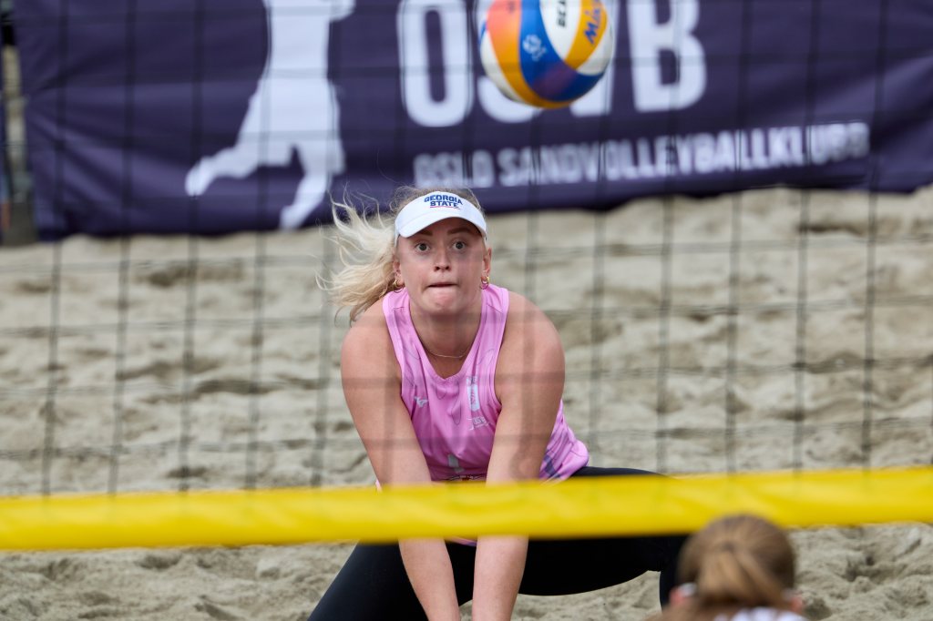 En sandvolleyballspiller i rosa topp utfører en fleksibel posisjon for å motta ballen under en kamp.