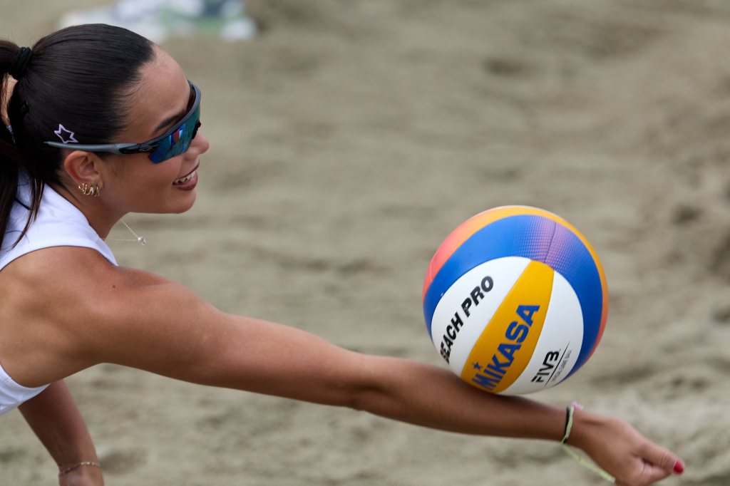 En kvinne som spiller beachvolleyball på sanden, smilende mens hun serverer ballen.