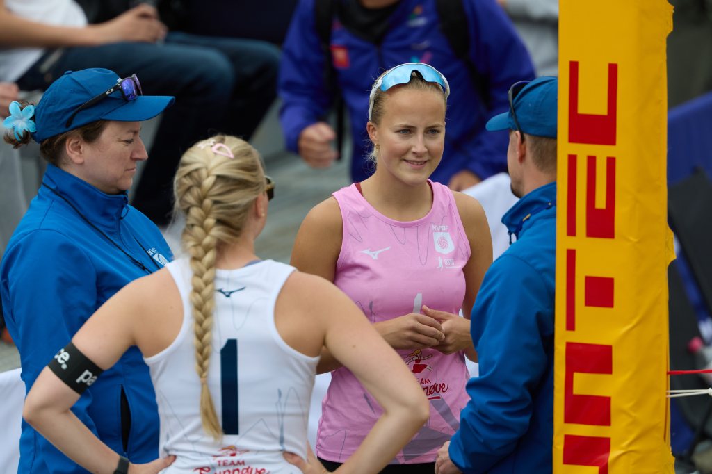 Fire personer i samtale før en sportsbegivenhet, en av dem iført en rosa treningsdrakt.