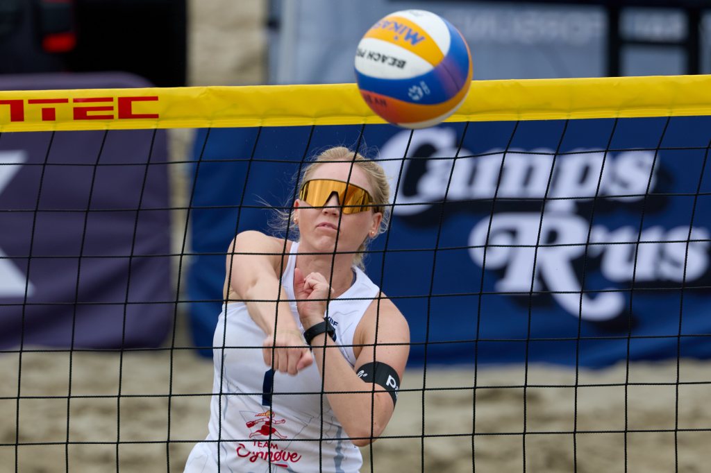 En atlet i sandvolleyball som står under nettet og forbereder seg på å motta ballen.