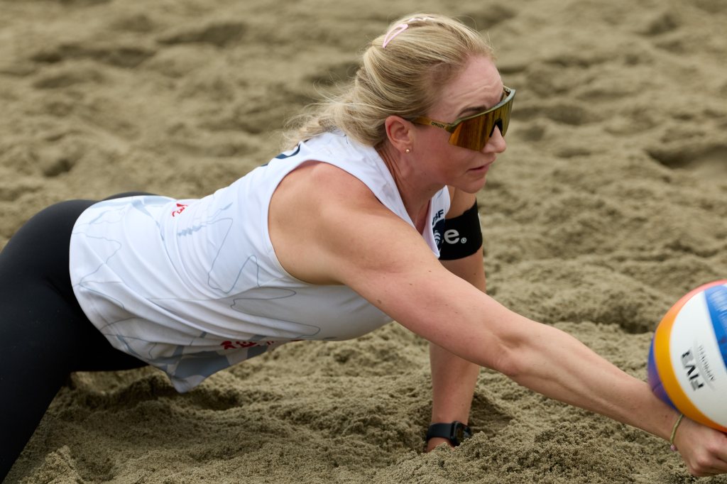 En kvinnelig sandvolleyballspiller som strekker seg for å nå en volleyball på en sandstrand.