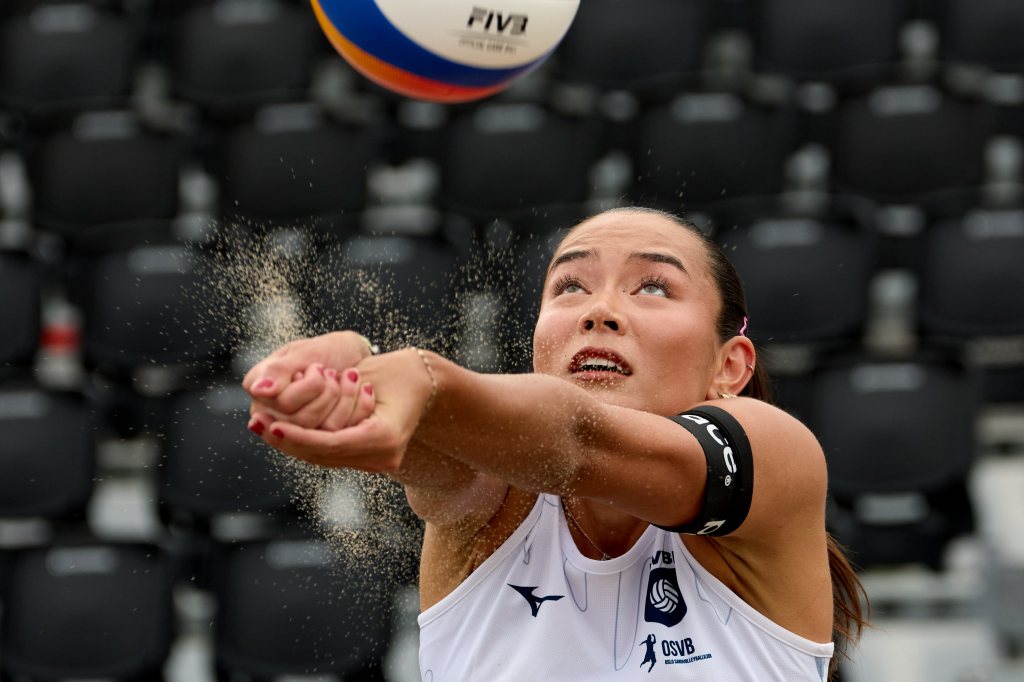 En kvinne som spiller sandvolleyball, med fokus på ballen og hennes utstrakte hender, omgitt av sand.