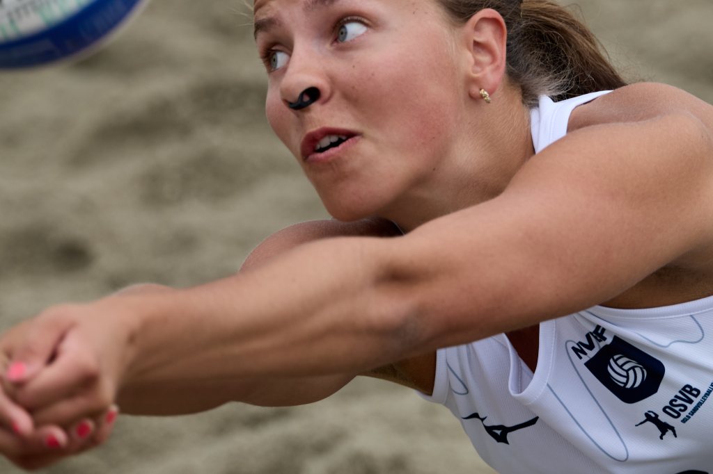 En kvinne som spiller beachvolleyball, som strekker seg etter en ball på sanden.