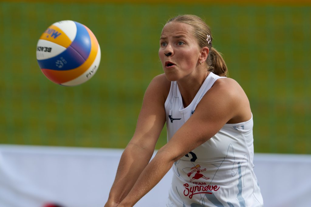 En kvinne i hvit sportsdrakt spiller volleyball og ser konsentrert ut mens hun tar imot ballen.