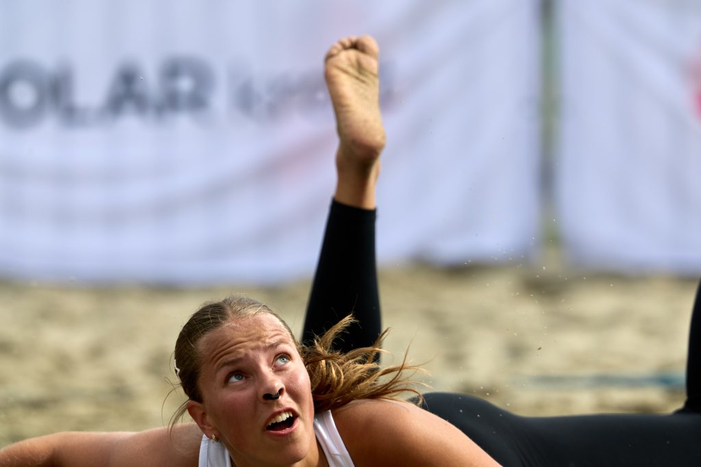 Kvinne som spiller sandvolleyball, liggende på bakken med et intenst uttrykk.