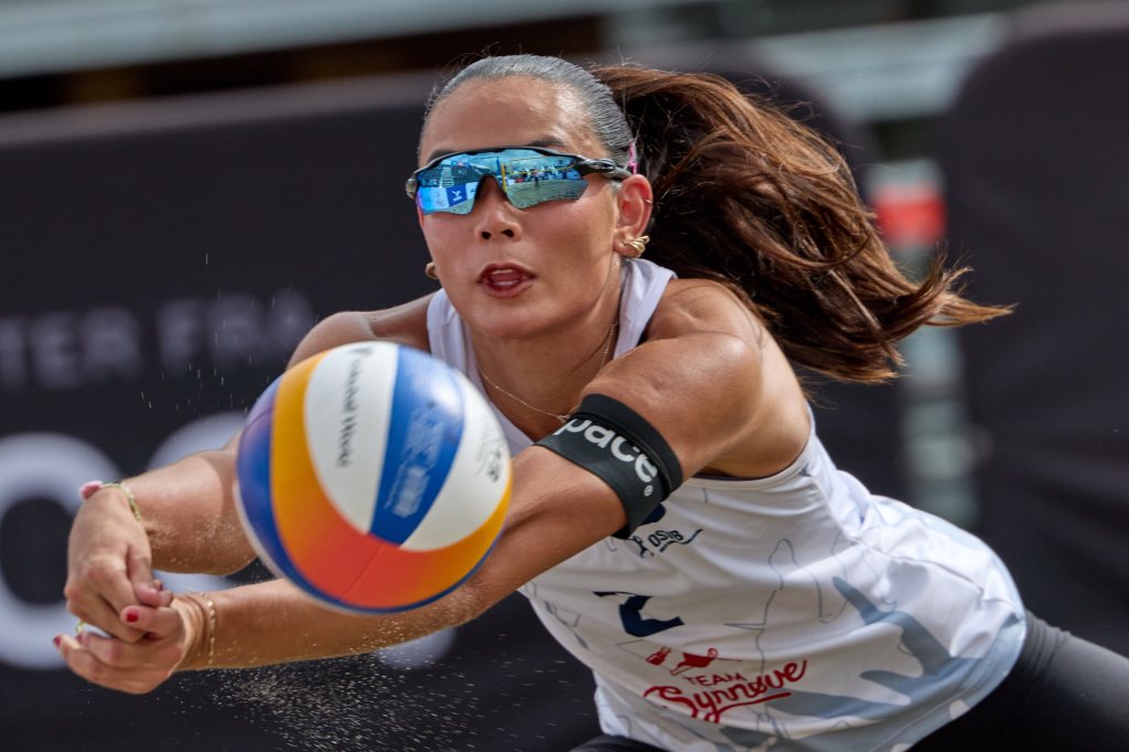 En kvinne i solbriller forbereder seg på å spille volleyball på stranden.