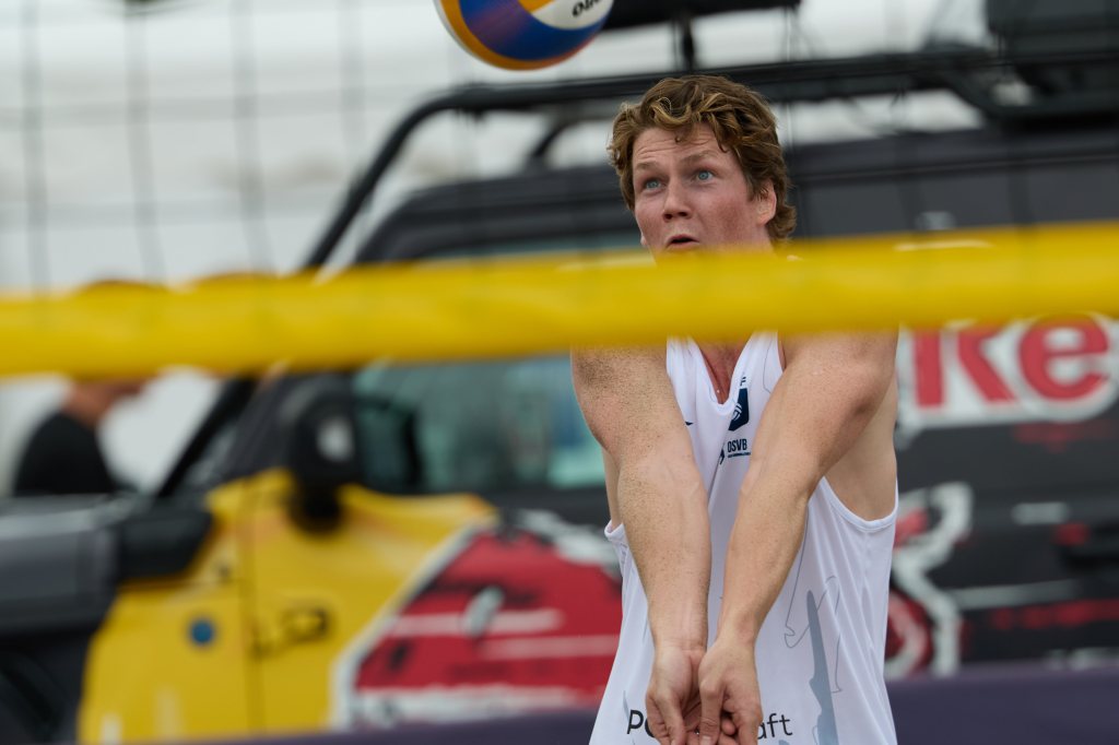 En ung mann spiller beachvolleyball, fokusert på å ta imot ballen som svever over nettet.