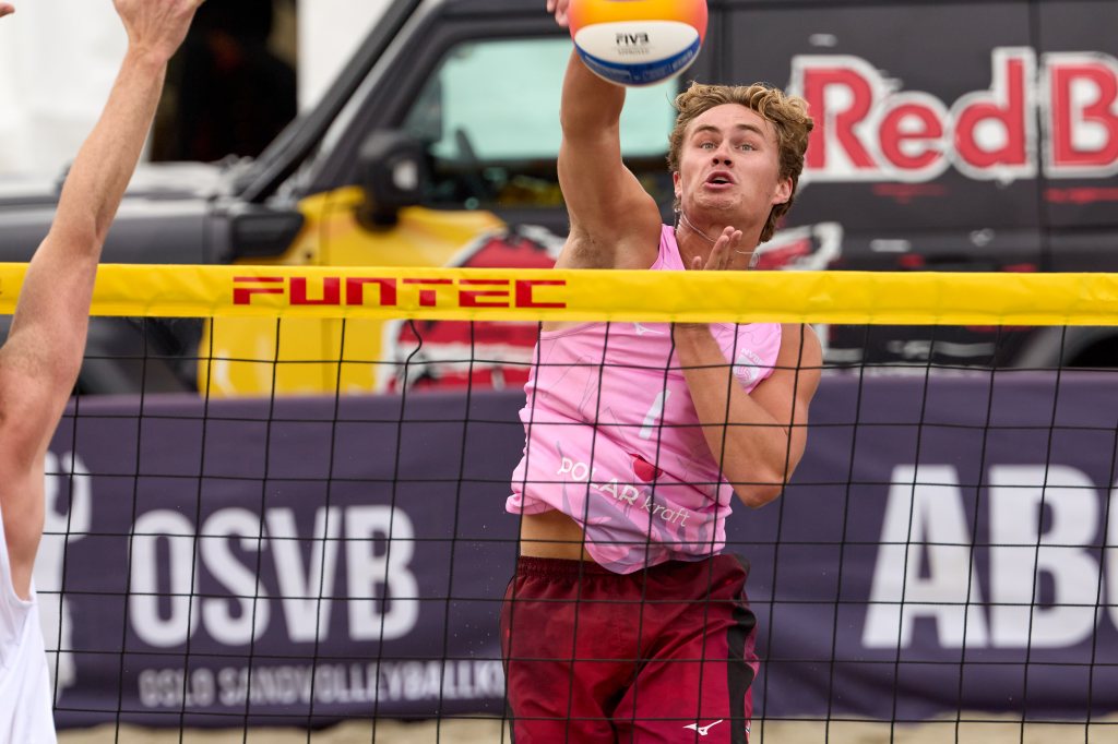 En volleyballspiller som hopper for å sprette ballen over nettet under en sandvolleyballkamp.
