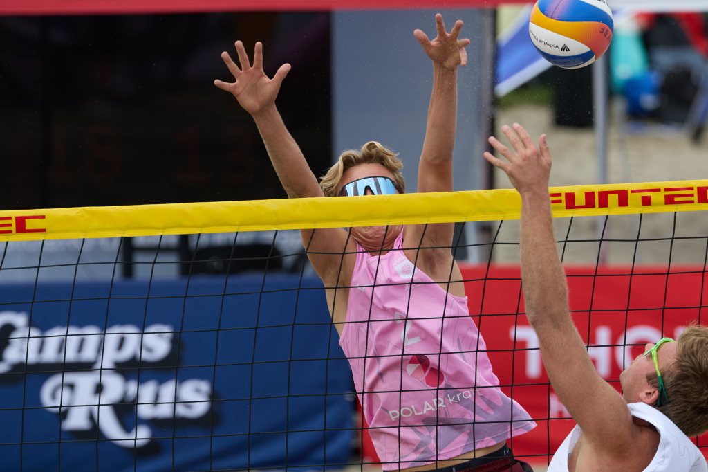 En strandvolleyballspiller hopper opp for å blokkere et skudd fra motstanderen over nettet.