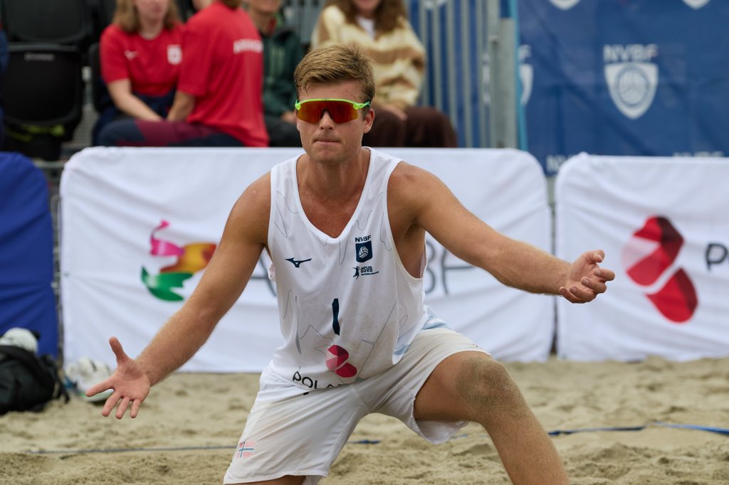 En beachvolleyballspiller i hvit drakt gestikulerer på banen, omgitt av publikum.