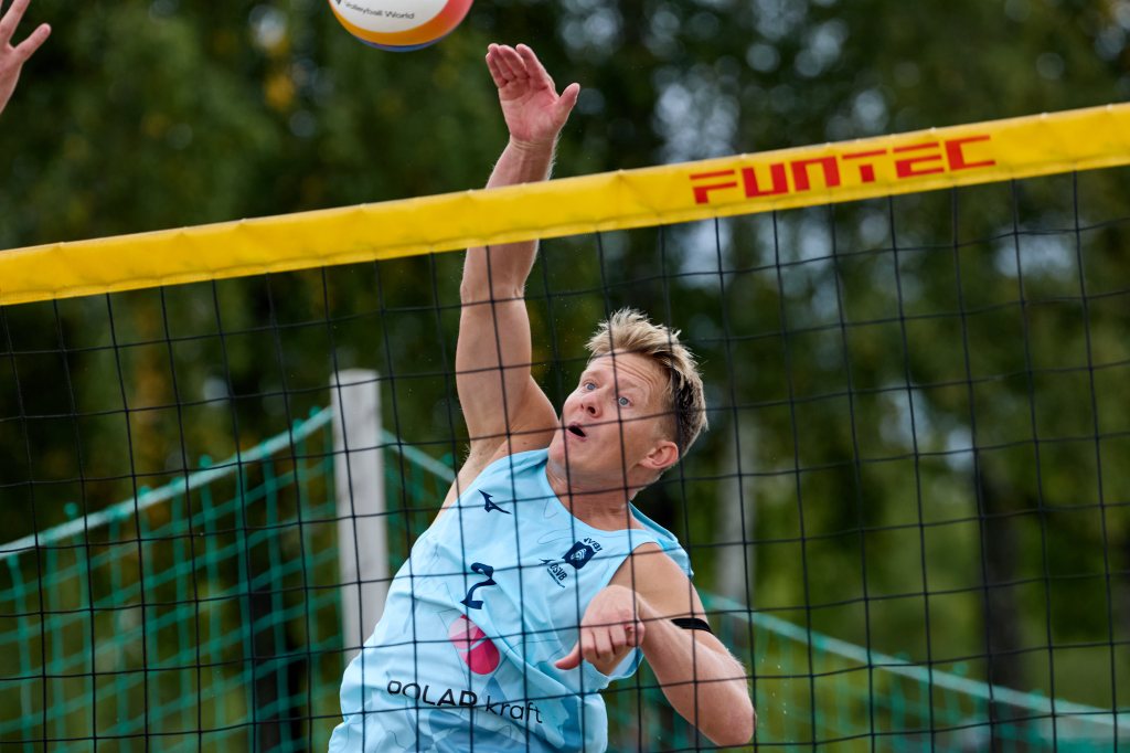 En volleyballspiller hopper for å utføre et angrep i sanden, med nettet og en volleyball i fokus.