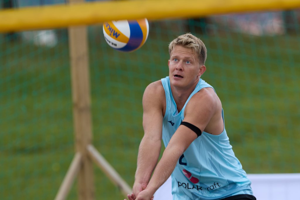 En volleyballdriver i blått antrekk forbereder seg på å ta imot en ball som flyr mot ham på en utendørs volleyballbane.