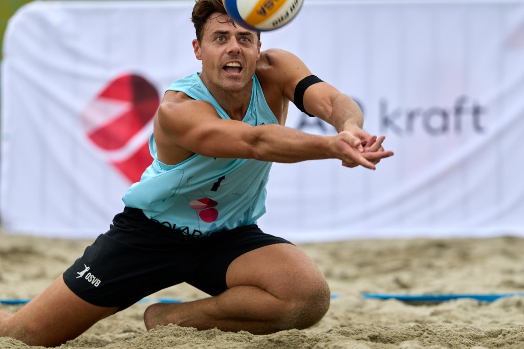 En beachvolleyballspiller som bøyer seg ned for å ta imot ballen på en sandbane.
