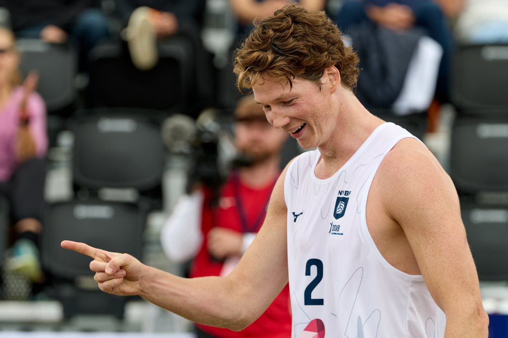 En glad volleyballspiller i hvit trøye med nummer to, smilende og peker med pekefingeren.
