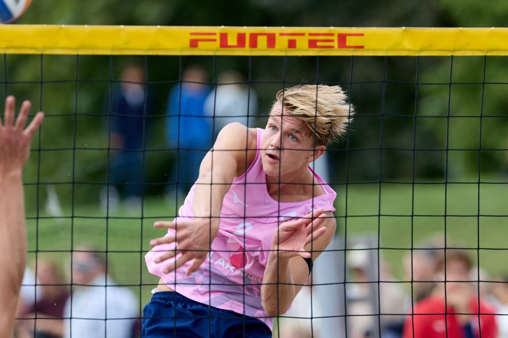 En volleyballspiller i rosa trøye gjør et angrep over nettet i en utendørs kamp.