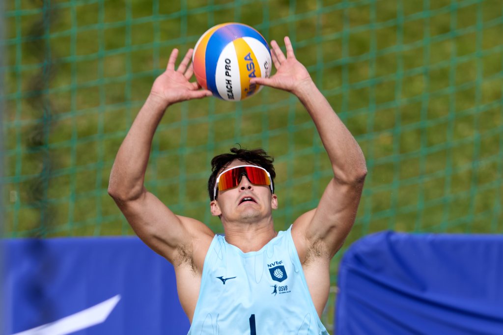 En beachvolleyballspiller i blått antrekk forbereder seg på å serve ballen under en konkurranse.