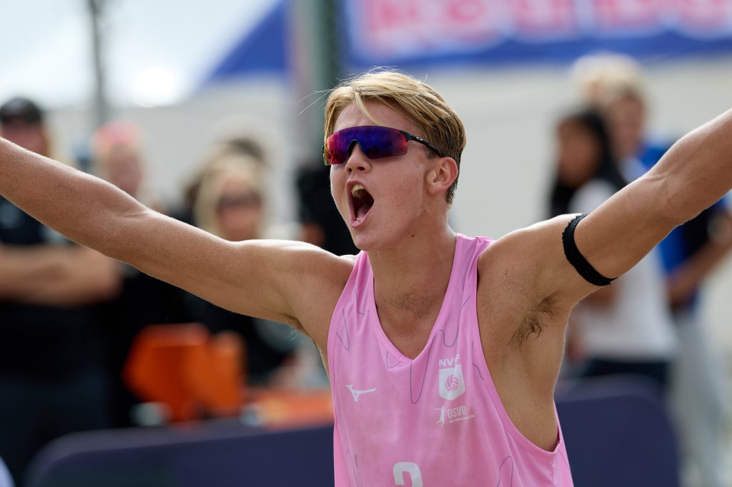 Ung mann i rosa sportsdrakt som jubler med armene hevet under en volleyballturnering.