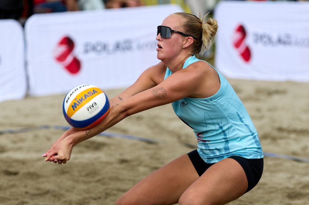 En strandvolleyballspiller i solbriller utfører en mottak av ballen på en sandbane.