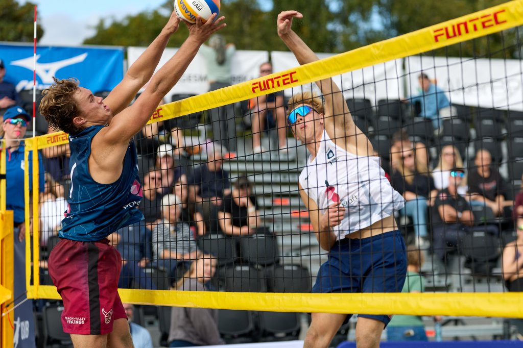 To beachvolleyballspillere i aksjon ved nettet, med publikum i bakgrunnen.