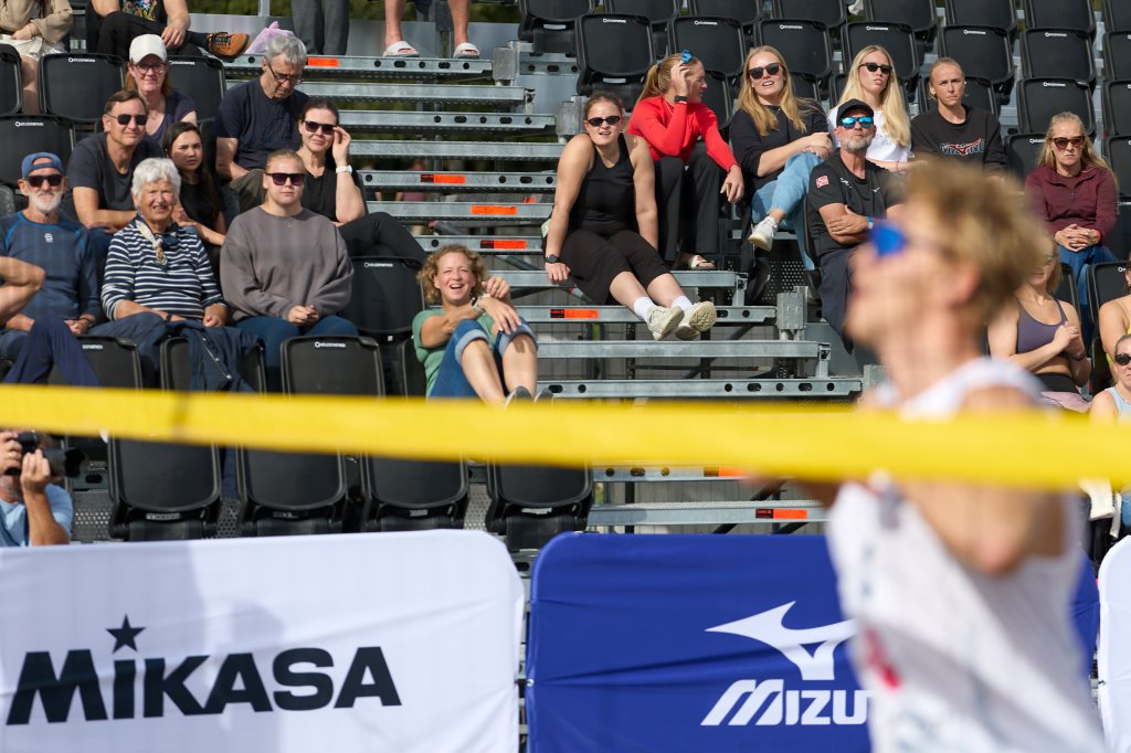 En gruppe tilskuere sitter på tribunene og ser på en sportsbegivenhet, med et fokus på en utøver i bevegelse foran dem.