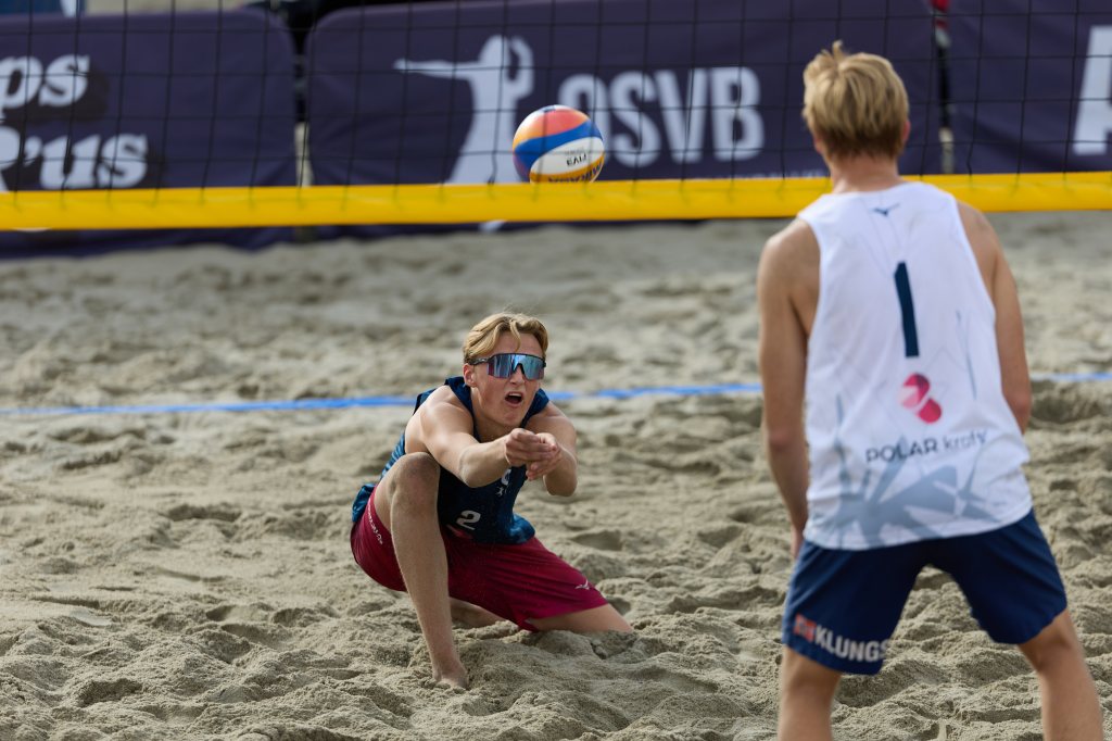 To unge spillere spiller sandvolleyball, en spiller er i ferd med å motta ballen.
