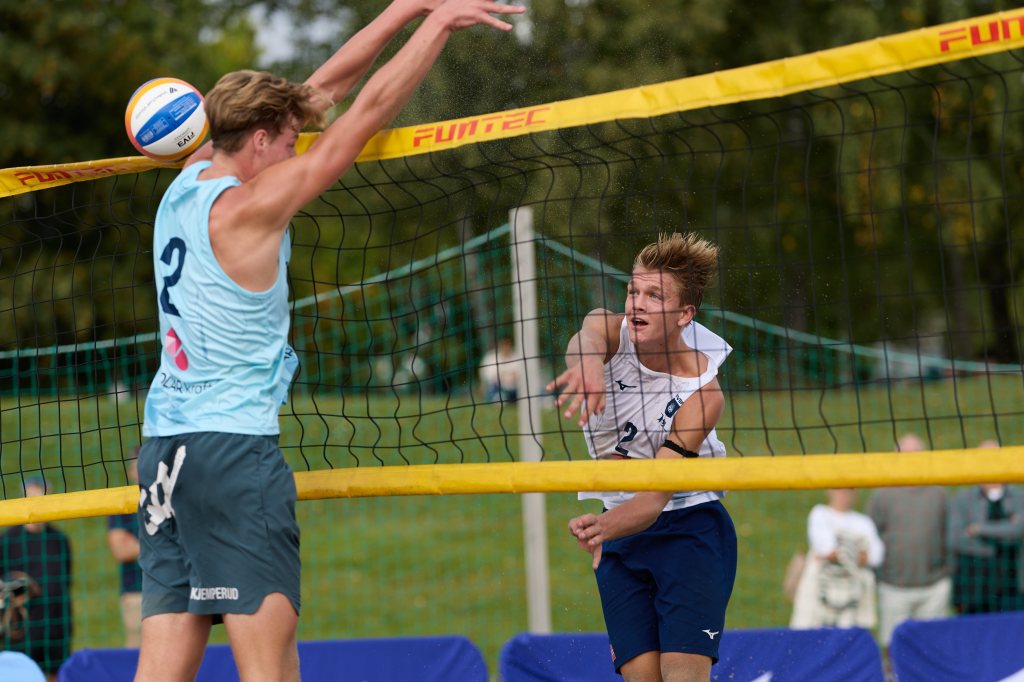 To unge menn spiller volleyball, hvor den ene hopper for å blokkere ballen som den andre slår.