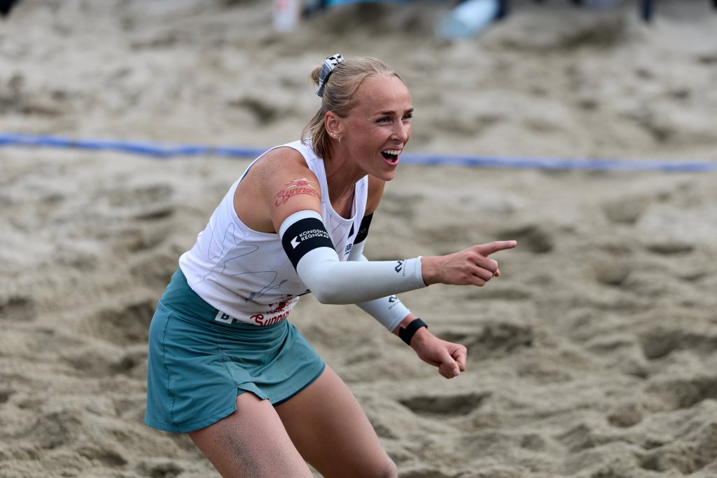 En kvinnelig beachvolleyballspiller jubler og peker mens hun står på sanden.