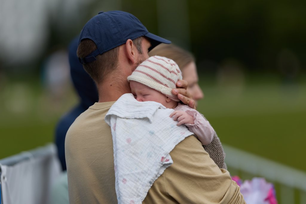 En far holder sin sovende baby i armene mens de ser på en utendørs begivenhet.