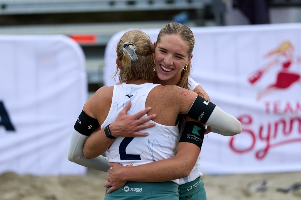 To beach volleyball-spillere omfavner hverandre etter en seier.
