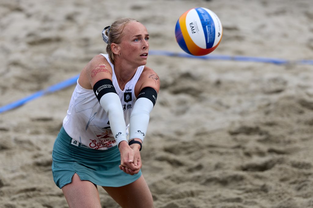 En kvinne spiller sandvolleyball og forbereder seg på å ta imot en ball i en sandbane.