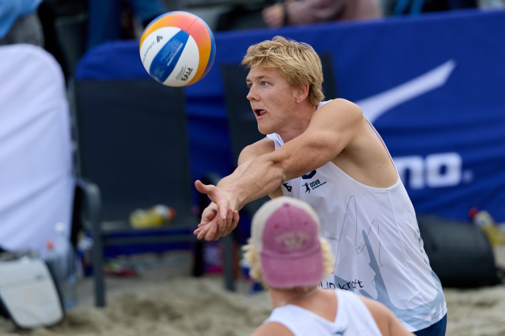 Ung mann i hvit tanktopp som spiller beachvolleyball, klar til å slå ballen.