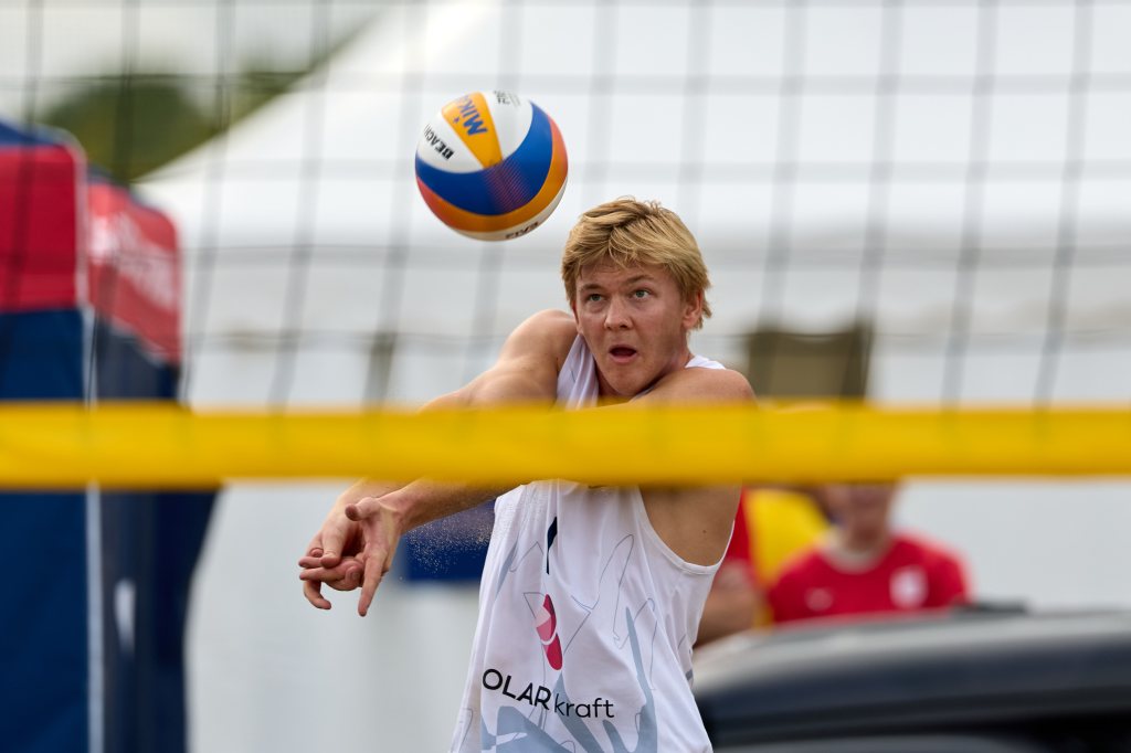 En ung mann spiller strandvolleyball, forbereder seg på å motta ballen som flyr mot ham.