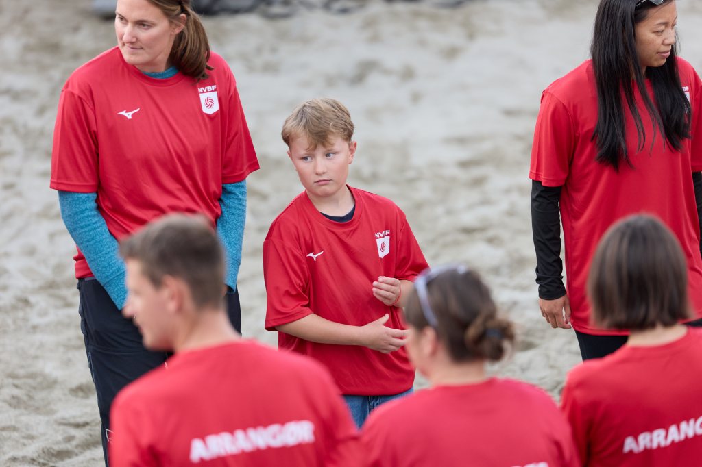 Gruppe mennesker iført røde t-skjorter på en sandstrand, med voksne og et barn i fokus.