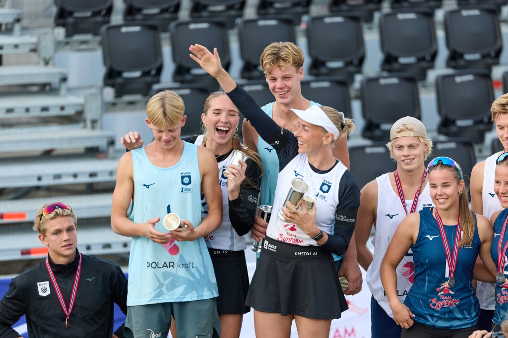 En gruppe unge utøvere feirer etter konkurransen, stående på et podium med trofeer og medaljer. De smiler og viser glede, med en kvinnelig utøver som hever en pokal.